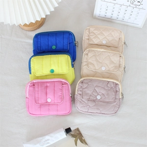 Vue à plat de mini pochettes matelassées colorées en bleu rose et jaune sur tissu blanc