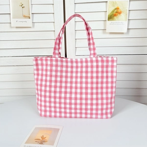 Detail view of a pink checkered canvas tote bag placed on a minimalist white desk