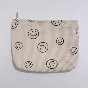Detailed view of beige corduroy pouch with black smiley prints and metal zipper