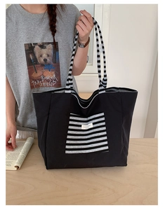 Detail of black canvas tote bag with striped front pocket and woven textile handles