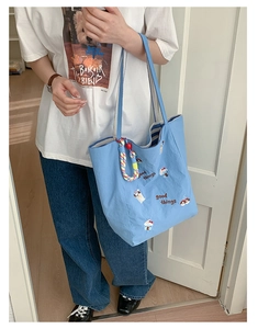 Détail du sac cabas en toile bleu clair avec broderie cartoon et breloque en corde tissée