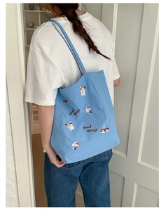 Détail de broderie chien de dessin animé et texte 'good things' sur un sac cabas bleu clair