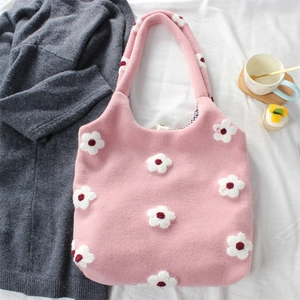 Pink knit tote bag with white flower details and plaid lining on a cozy textile background