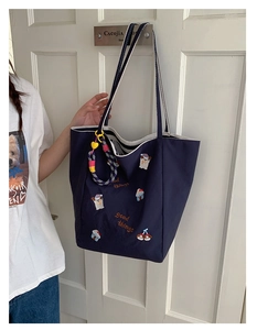 Détail du cabas en toile marine avec broderies de dessins animés et anses rayées