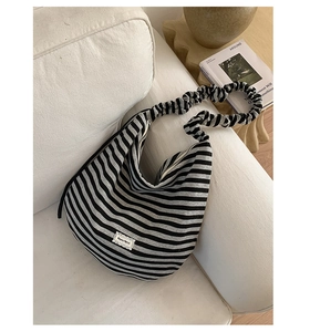 Detail of striped canvas hobo bag with ruffled scrunchie strap on a beige sofa