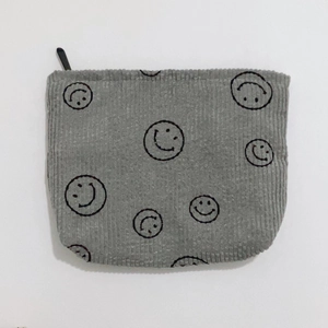 Close-up of grey corduroy makeup bag featuring black smiley face pattern and zipper