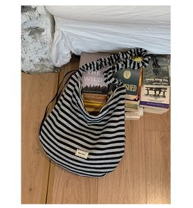 Detail view of the black striped bag featuring unique scrunched shoulder strap on wood floor