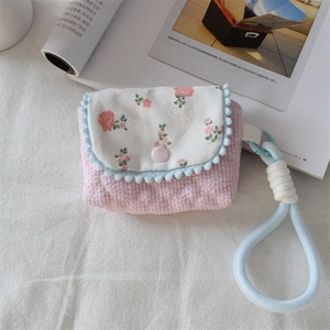 Detail view of quilted floral camera case with blue pom-poms and woven handle strap