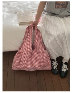 Detail of red and white checkered tote bag with blue embroidery on a minimalist bed