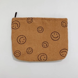 Close-up of brown corduroy pouch with black smiley face pattern and zipper detail