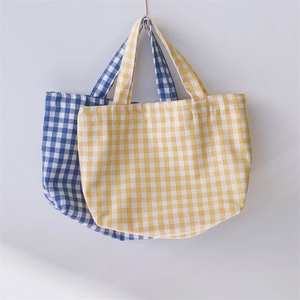 Detail of checkered canvas tote bags in yellow and blue hanging against a white wall