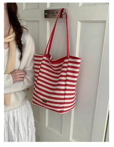 Détail du sac cabas en toile rayé rouge et blanc avec logo accroché à une porte blanche