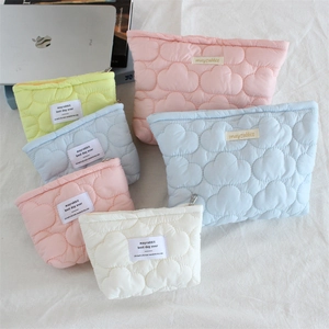 Quilted pastel clouds makeup bag with zipper and logo label on a minimalist desk