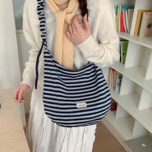 Blue and white striped crossbody bag with adjustable strap worn by model in cozy setting