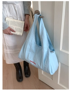 Detail of light blue tote bag with red GoodThing text hanging on white door