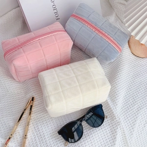 Close-up of quilted plush pouches in pink, grey-blue and cream with top zipper detail