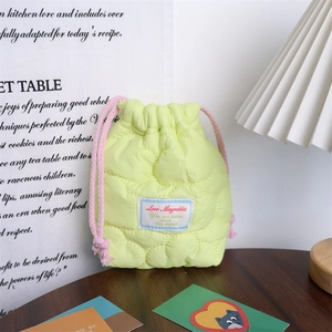 Detail of a quilted yellow drawstring pouch with heart stitching on a wooden surface