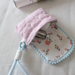 Detailed view of floral lining and blue pom-pom trim on small quilted camera pouch