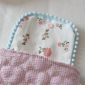 Detail of floral camera pouch showing pink snap button, blue pom pom trim and quilted texture