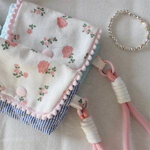 Floral fabric storage bag with pink pompom trim and adjustable braided strap