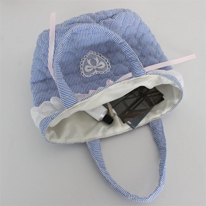 Detail of blue striped quilted bucket bag showing lace trim and pink ribbon bow