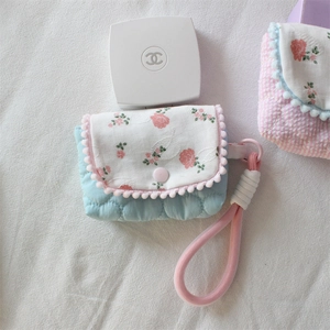 Detail of blue quilted camera case with floral flap and pink pom-pom trim and lanyard