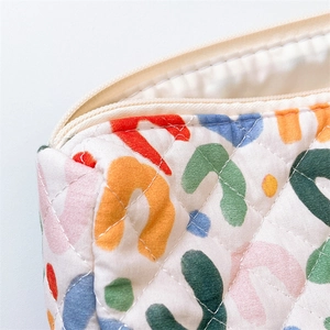 Close-up of diamond quilted fabric with colorful abstract patterns and cream zipper detail