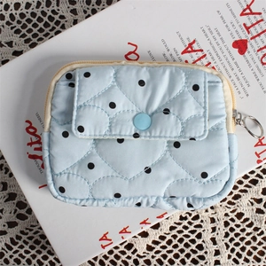 Détail de la pochette matelassée en cœur bleu clair à pois noirs avec bouton-pression