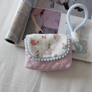 Detail of floral embroidery and blue pom-pom trim on a quilted fabric camera pouch