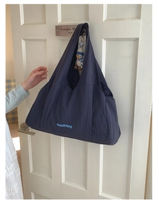 Detail of navy blue nylon tote bag with GoodThing logo hanging on a white wooden door
