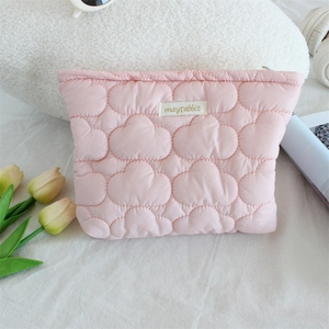 Close-up of quilted pink cloud makeup bag with brand label on soft fabric background