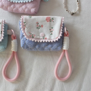 Detailed close-up of a floral quilted camera pouch with pink pom-pom trim and striped base