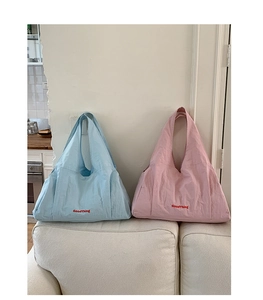 Detailed view of light blue and pink nylon tote bags with GoodThing slogan on a sofa