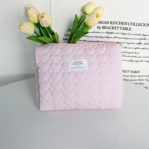 Detailed view of pink quilted heart pattern toiletry bag with white logo and zipper