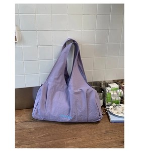 Detail of purple nylon tote bag with GoodThing logo and wrinkled texture on wood surface