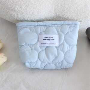 Close-up of light blue quilted makeup bag featuring cloud patterns and woven brand label