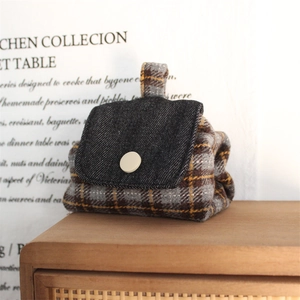 Detail of plaid fabric coin purse with blue denim flap and white button on wooden shelf