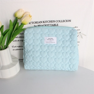 Close-up of light blue heart-quilted makeup bag with brand label and tulip background