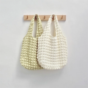 Detail of popcorn textured tote bags in light green and cream on a wooden rack