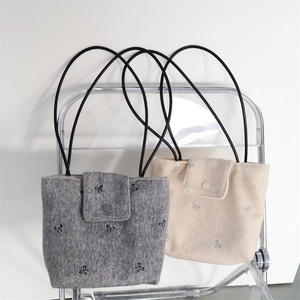 Detail of embroidered bow patterns on textured grey and beige canvas tote bags