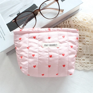Pink quilted cosmetic bag with red heart pattern and soft texture on a lace tablecloth