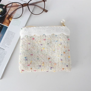 Detail of tweed coin purse with white lace trim and a pearl zipper pull on a desk