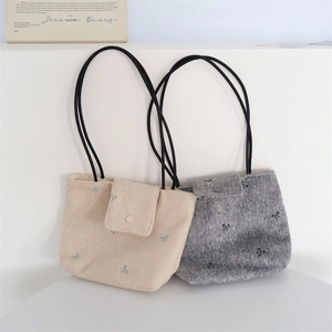Detail of bow-embroidered canvas tote bags in beige and grey with black cord straps