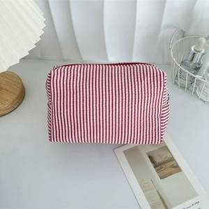 Macro detail of red and white striped seersucker makeup bag with zipper on a desk