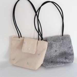 Close-up of embroidered bow detail and textured felt fabric on minimalist tote bags