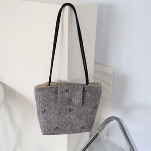 Detail of grey wool tote bag featuring black bow embroidery and flip-top button closure