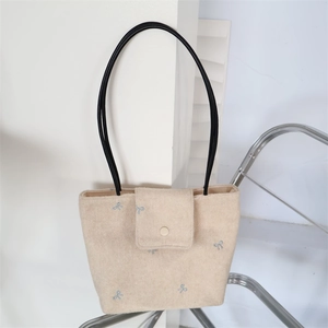Detail of beige plush tote bag with blue bow embroidery and sleek black shoulder straps