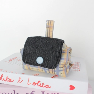 Close-up of a plaid canvas coin purse with a denim flap and button on stacked books