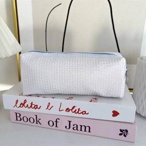 Close-up of white seersucker pencil case with blue zipper and metal pull on books