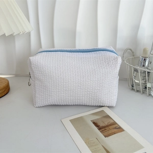 Detail view of white seersucker waffle texture bag with a blue zipper and metal ring pull